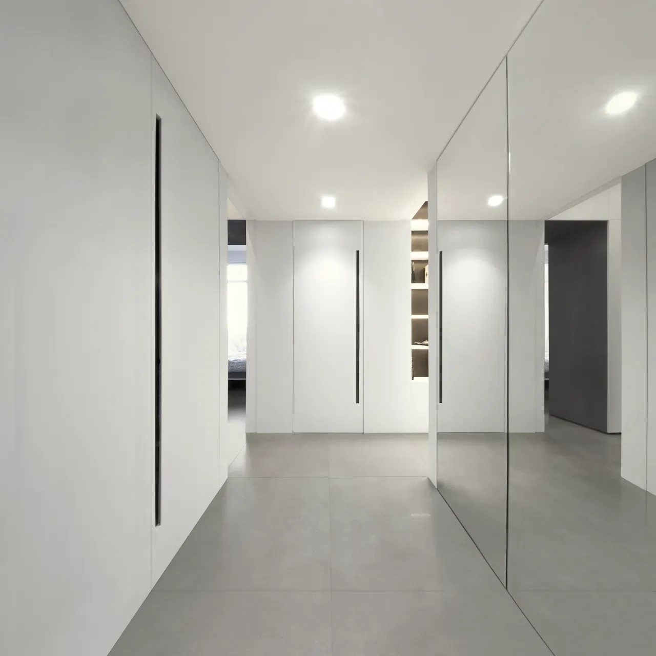 Hallway with white flush storage walls, a mirrored panel and grey floor tiles