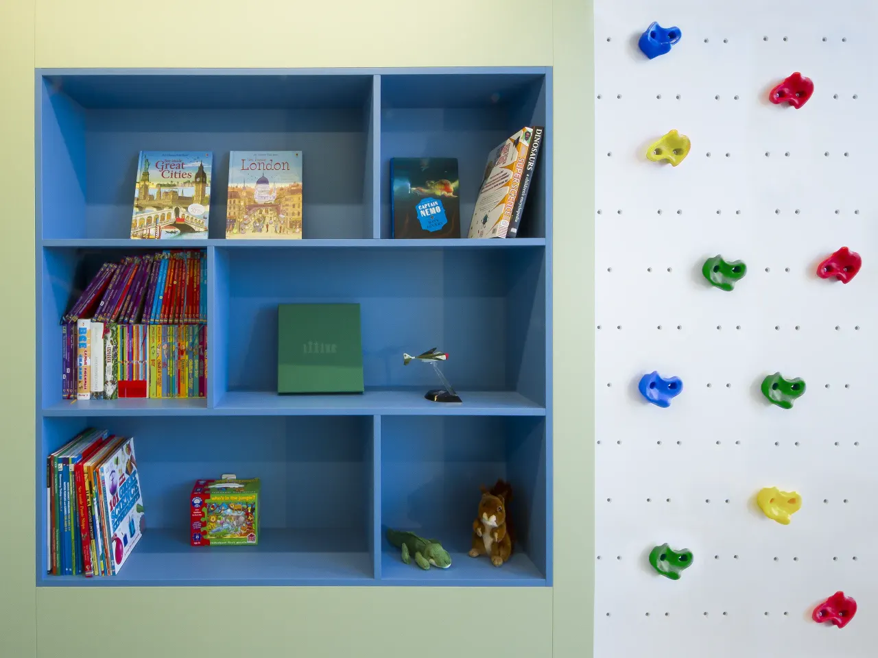 Blue built-in bookcase beside a white wall with colourful climbing holds