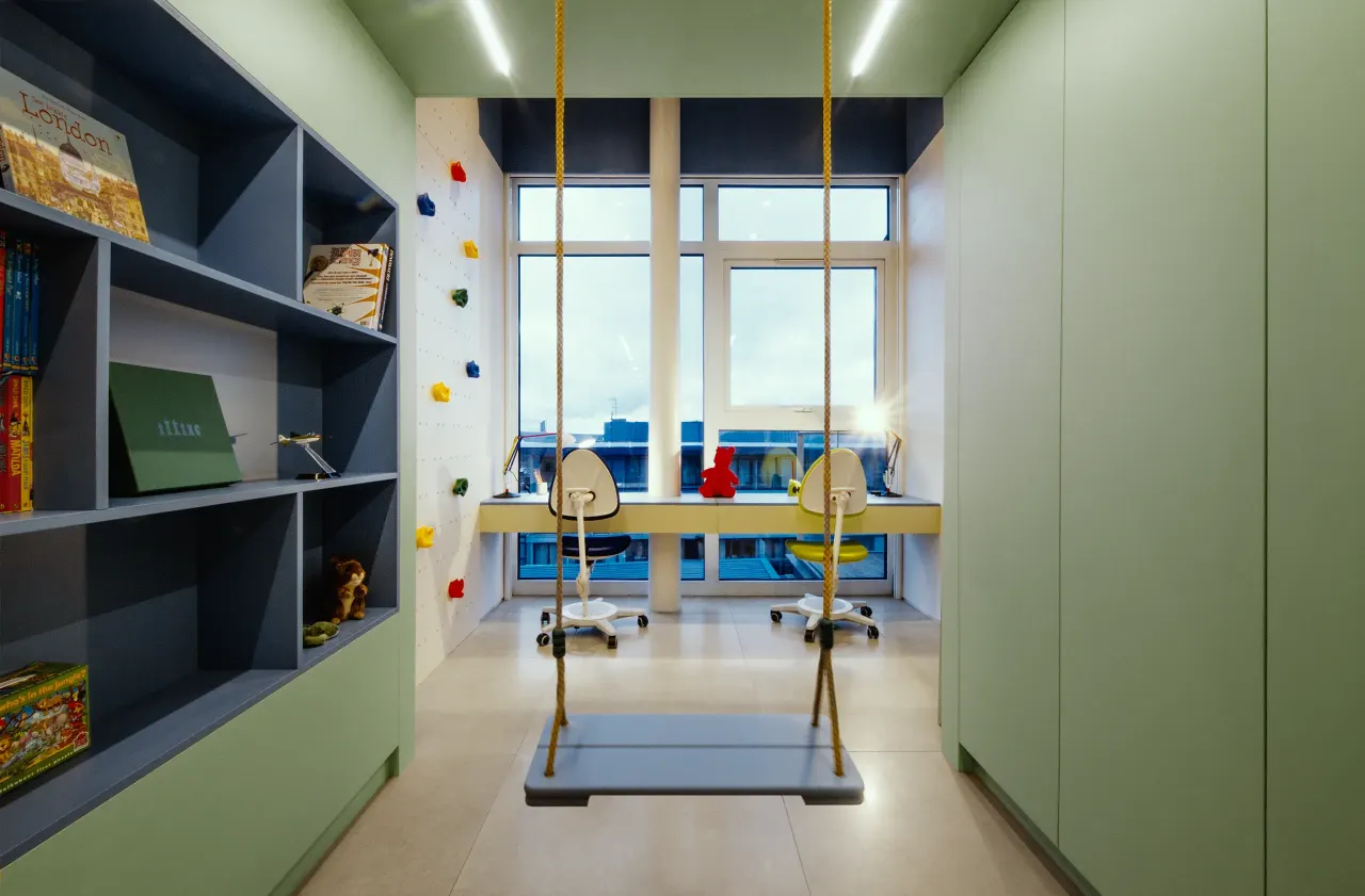 Children's room with a swing, blue bookshelves, green cabinets and desks by the window
