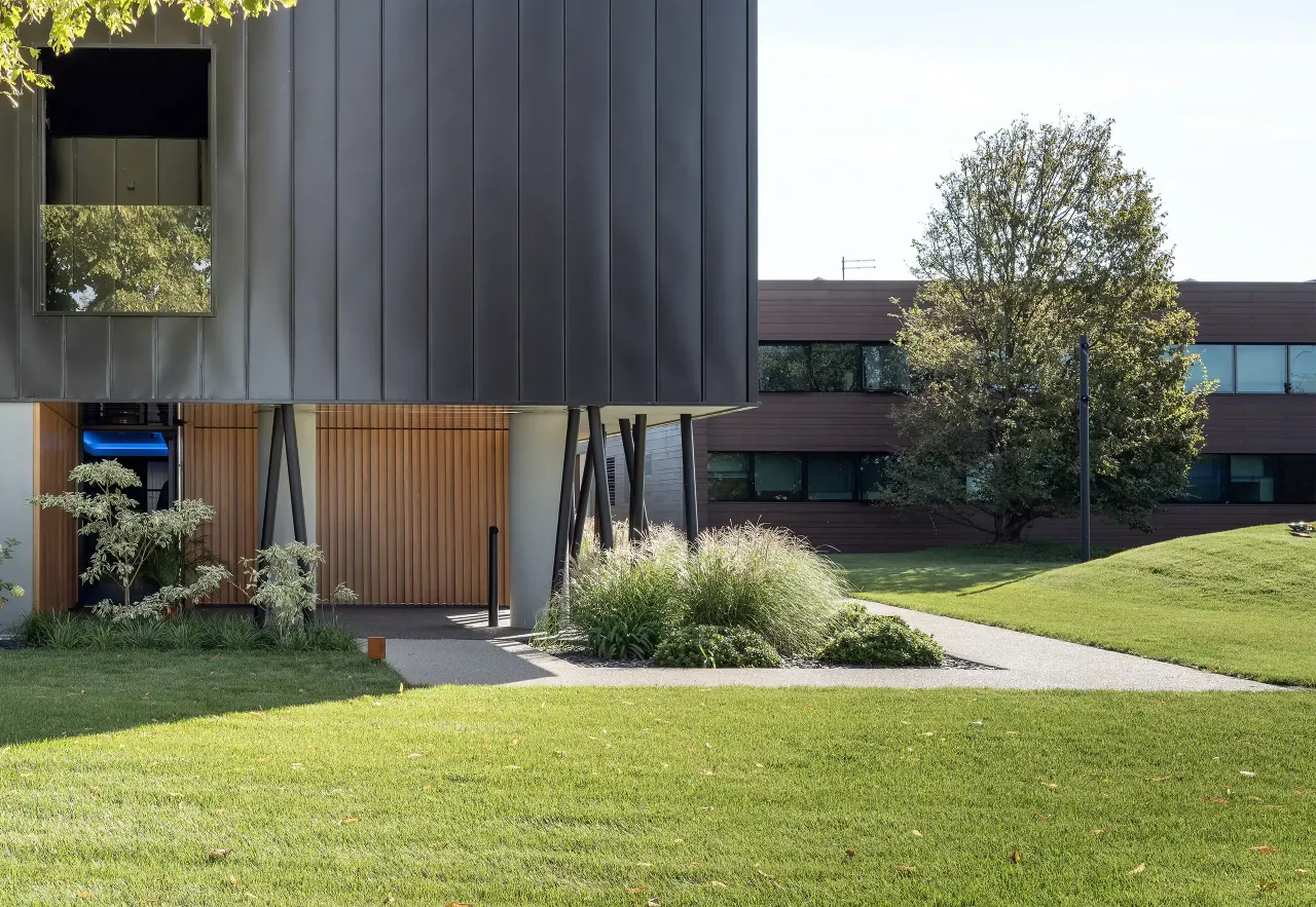 Overhanging dark volume above a landscaped entrance and lawn
