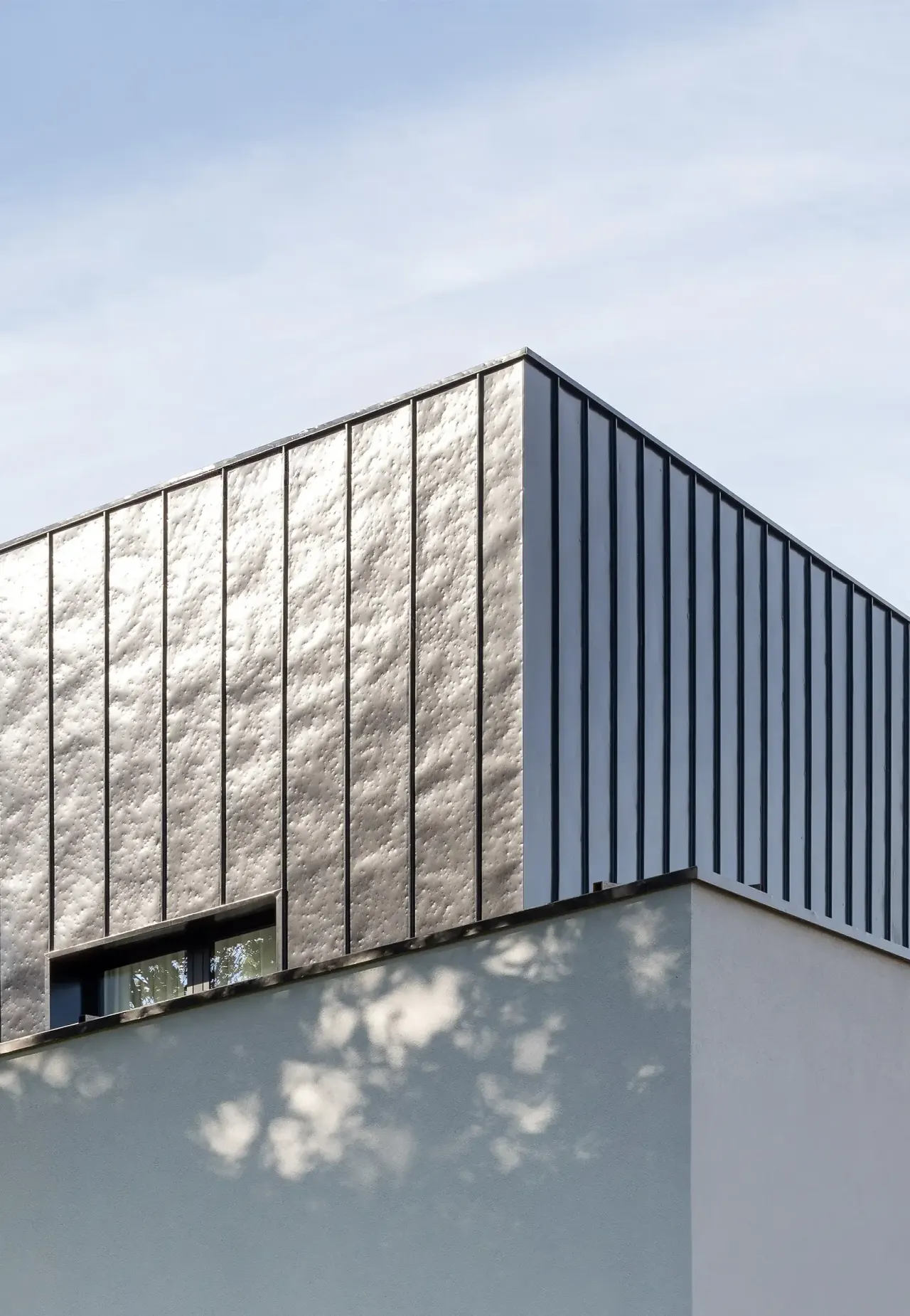 Corner of the textured metal facade above a white rendered wall