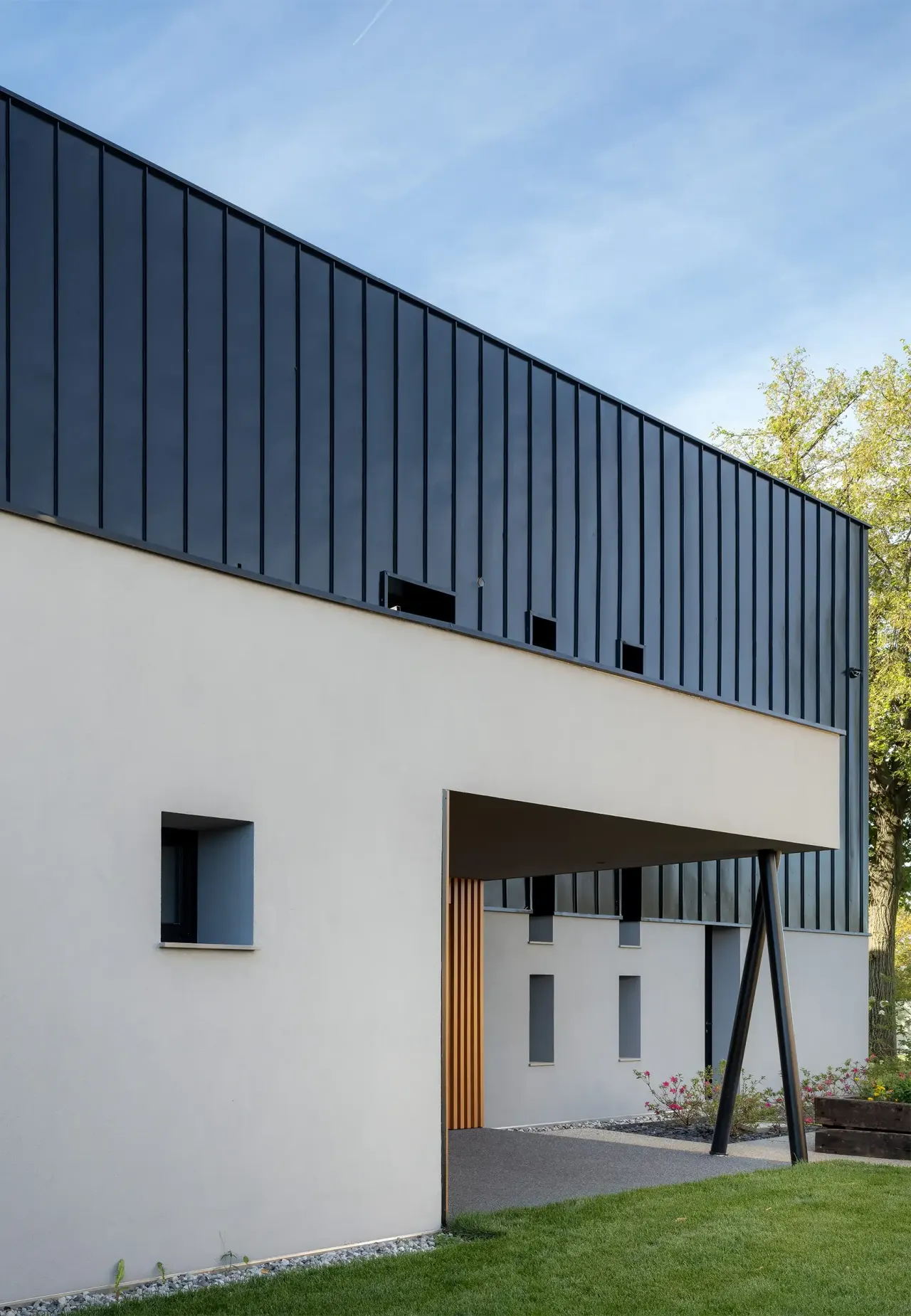 White rendered wall with small windows under the dark metal-clad upper floor