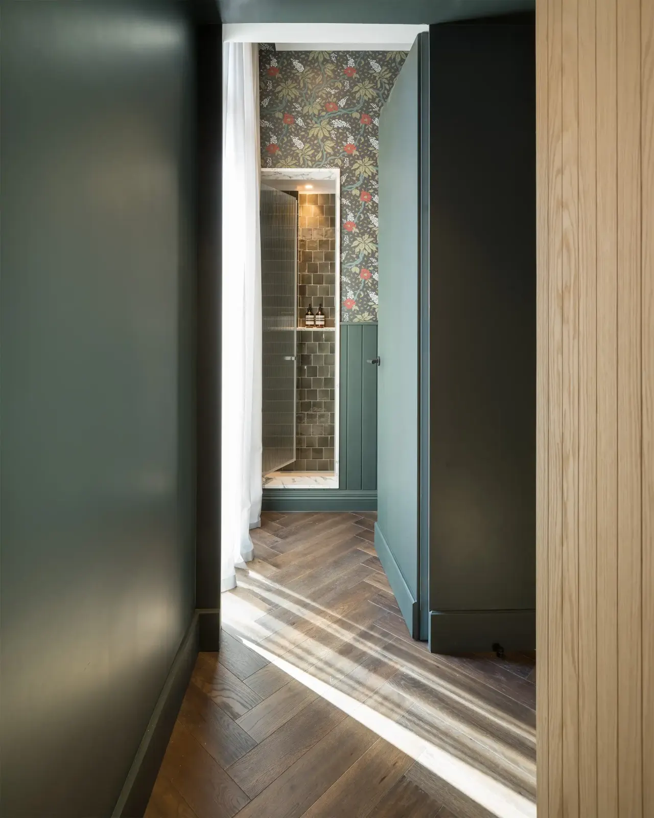 Dark green corridor leading to a bathroom with patterned wallpaper
