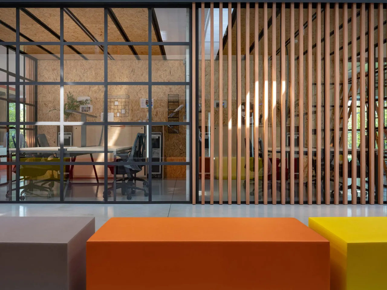 Black-framed glazed offices behind timber slats and coloured benches