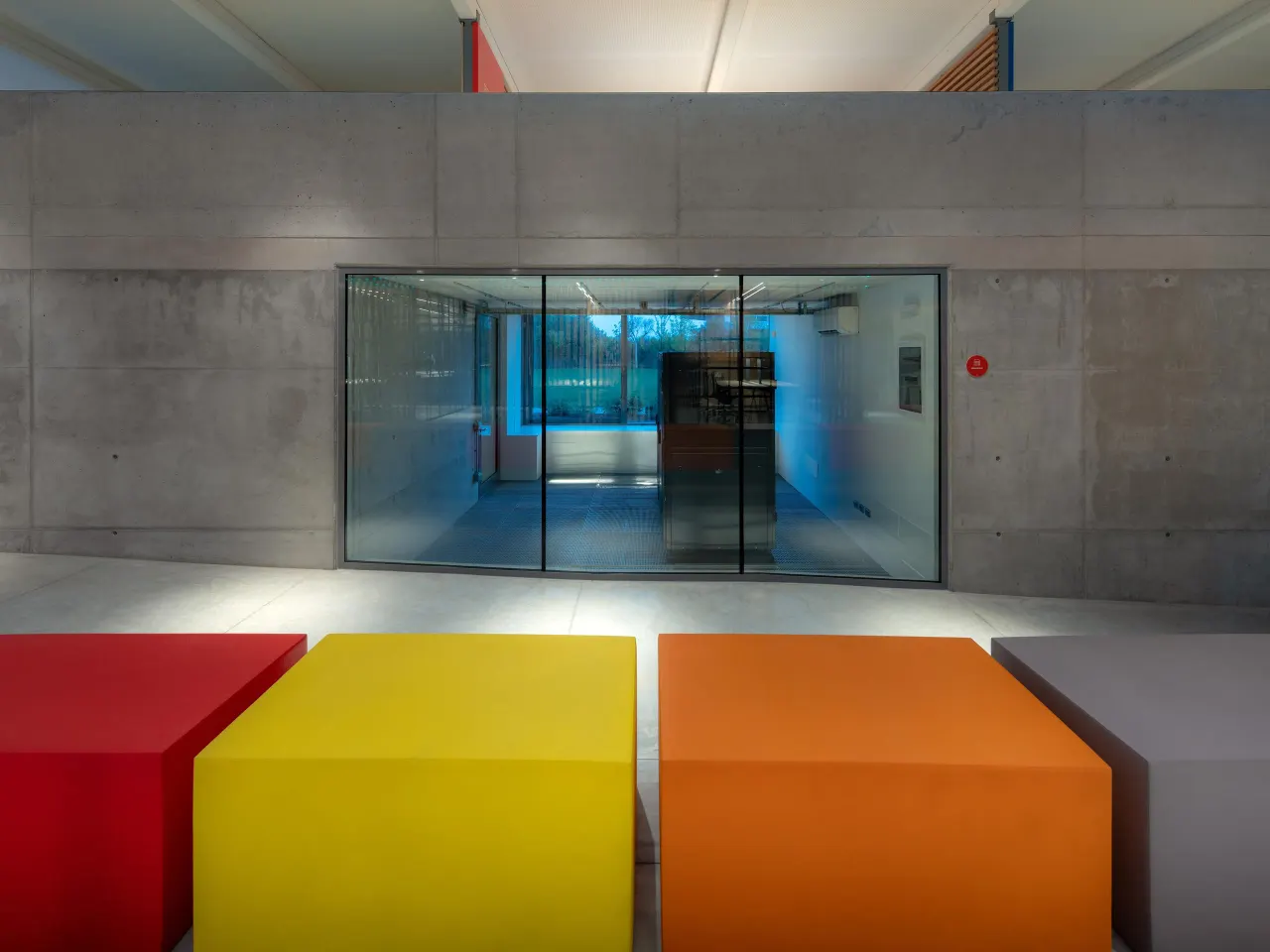 Red, yellow and orange benches in front of a concrete wall with a glazed room