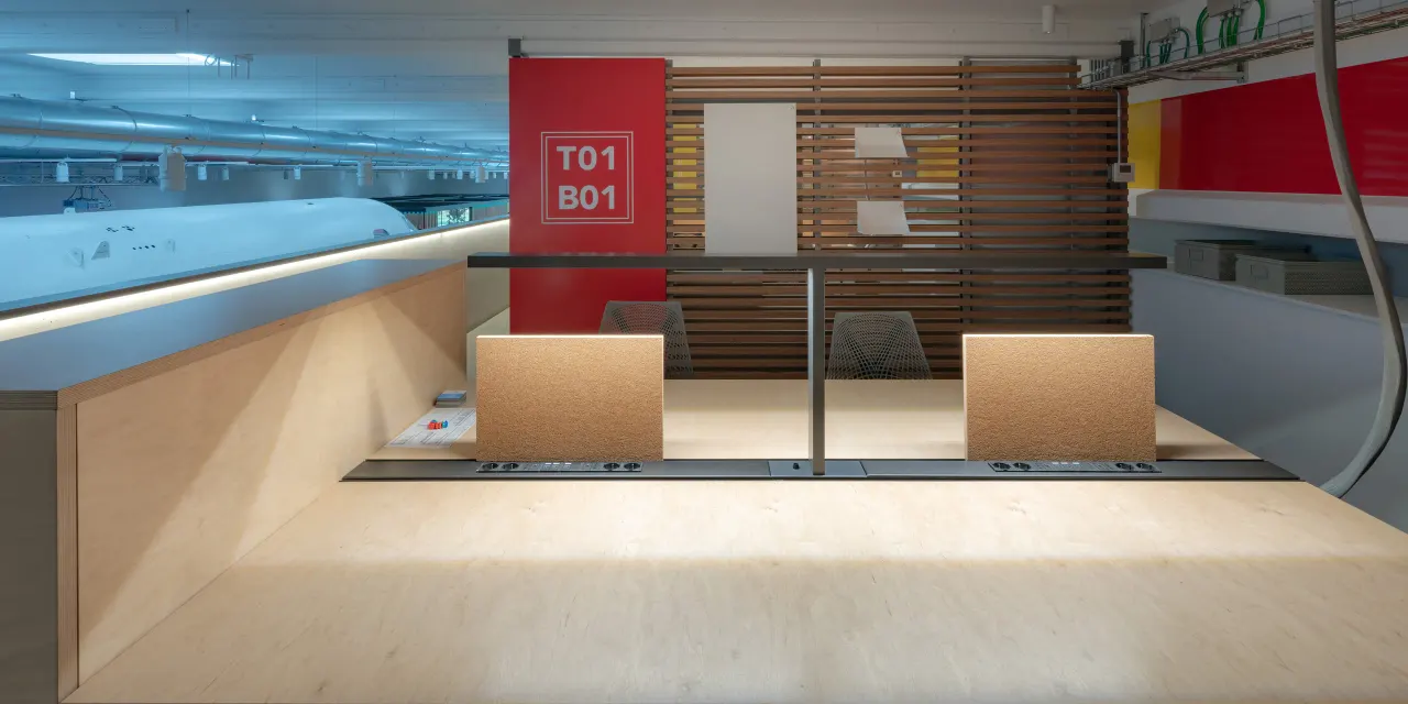 Plywood workstations beside a wall marked with wayfinding graphics