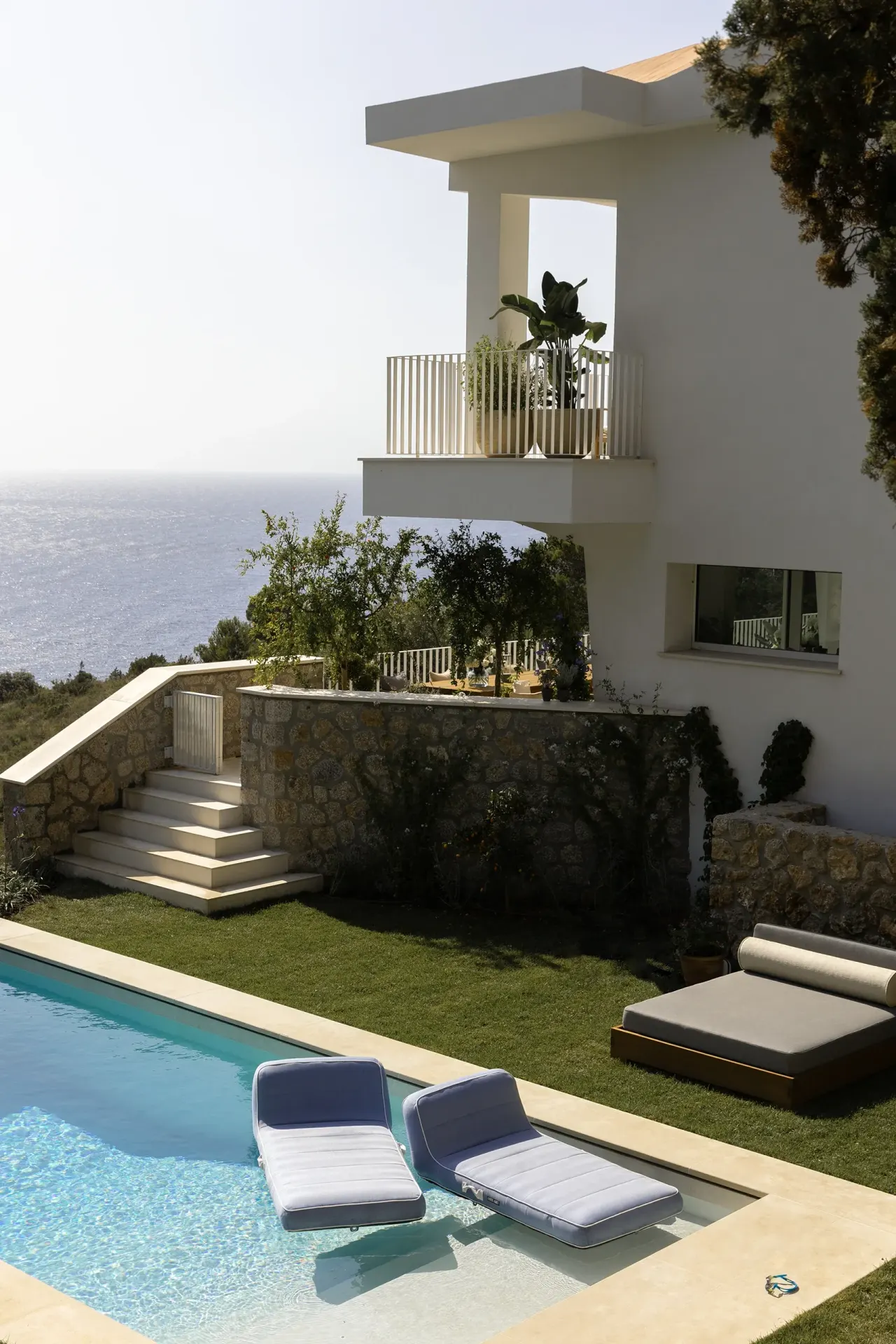 Swimming pool and sun loungers below the white villa and its balconies