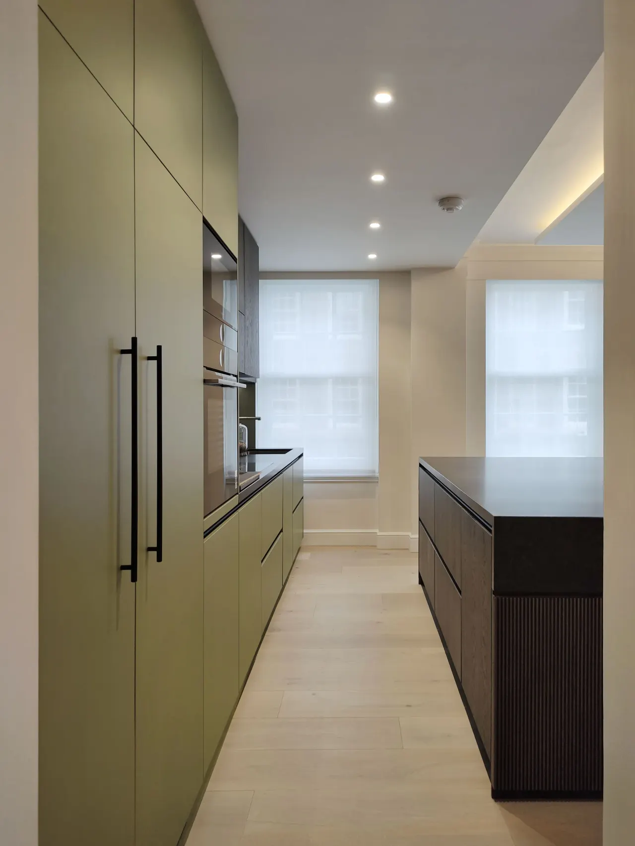 Galley kitchen with olive green tall units and a dark island