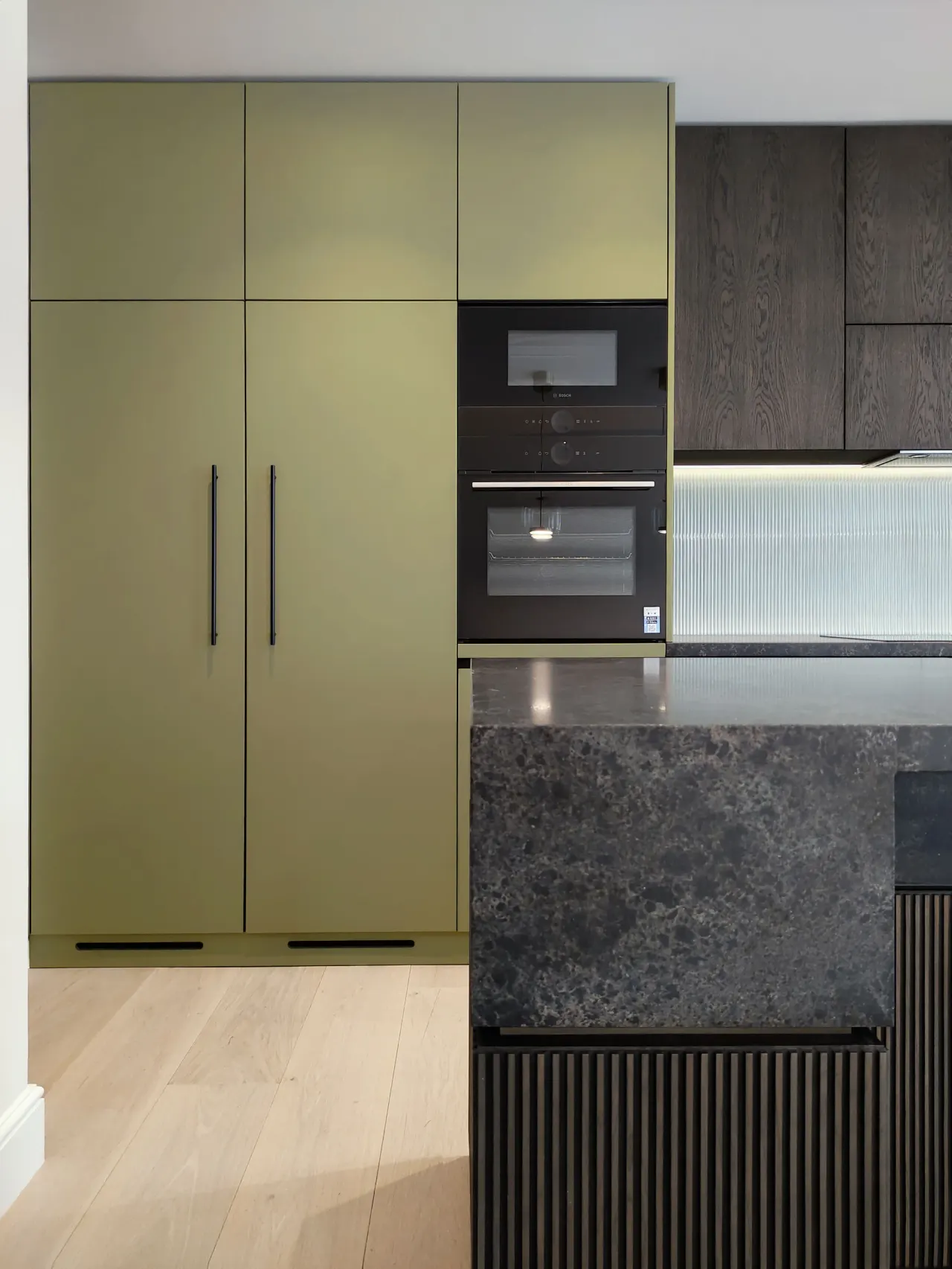 Olive green kitchen units, built-in ovens and stone-topped island
