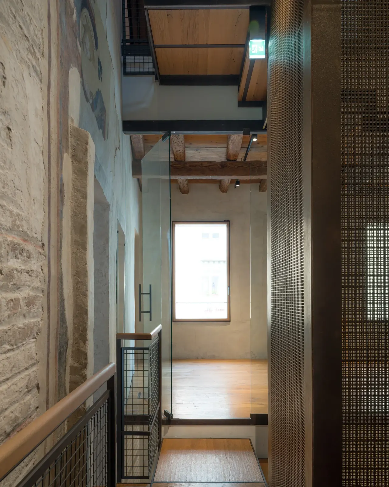Upper landing with perforated metal screens beside an exposed brick wall