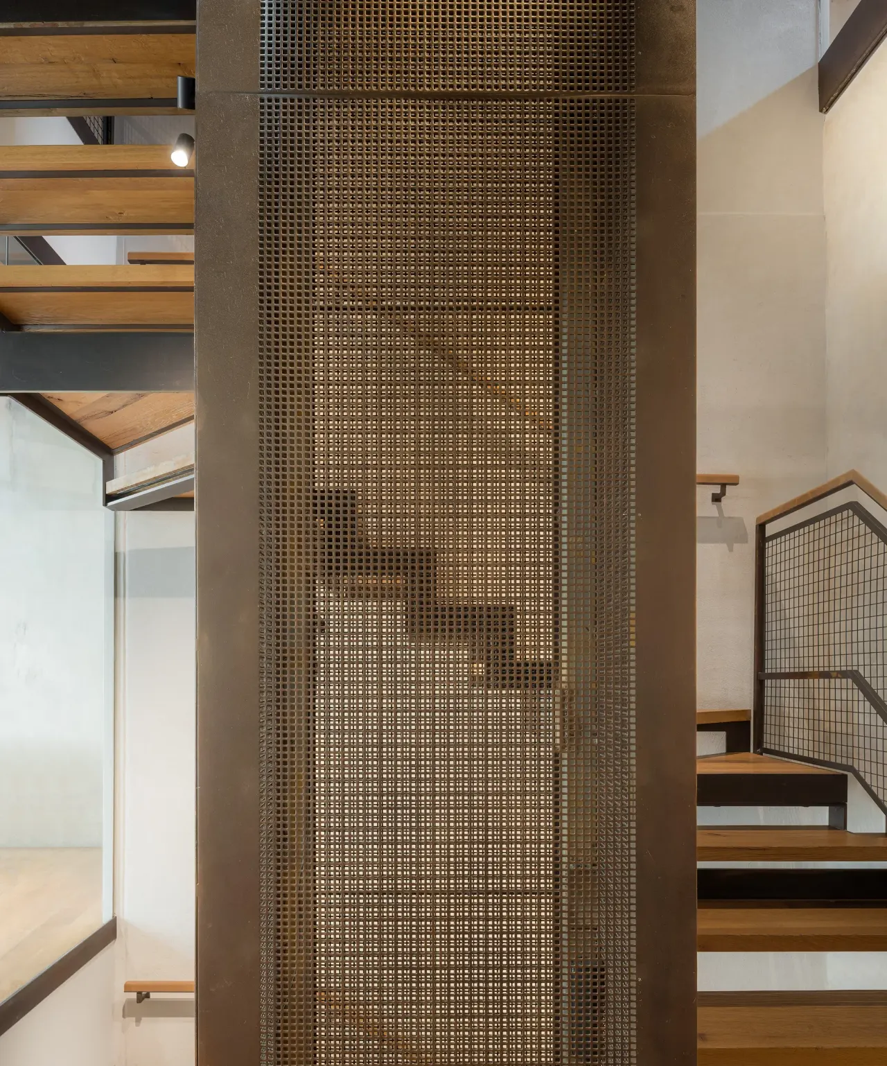 Staircase enclosed by a perforated bronze-coloured metal screen