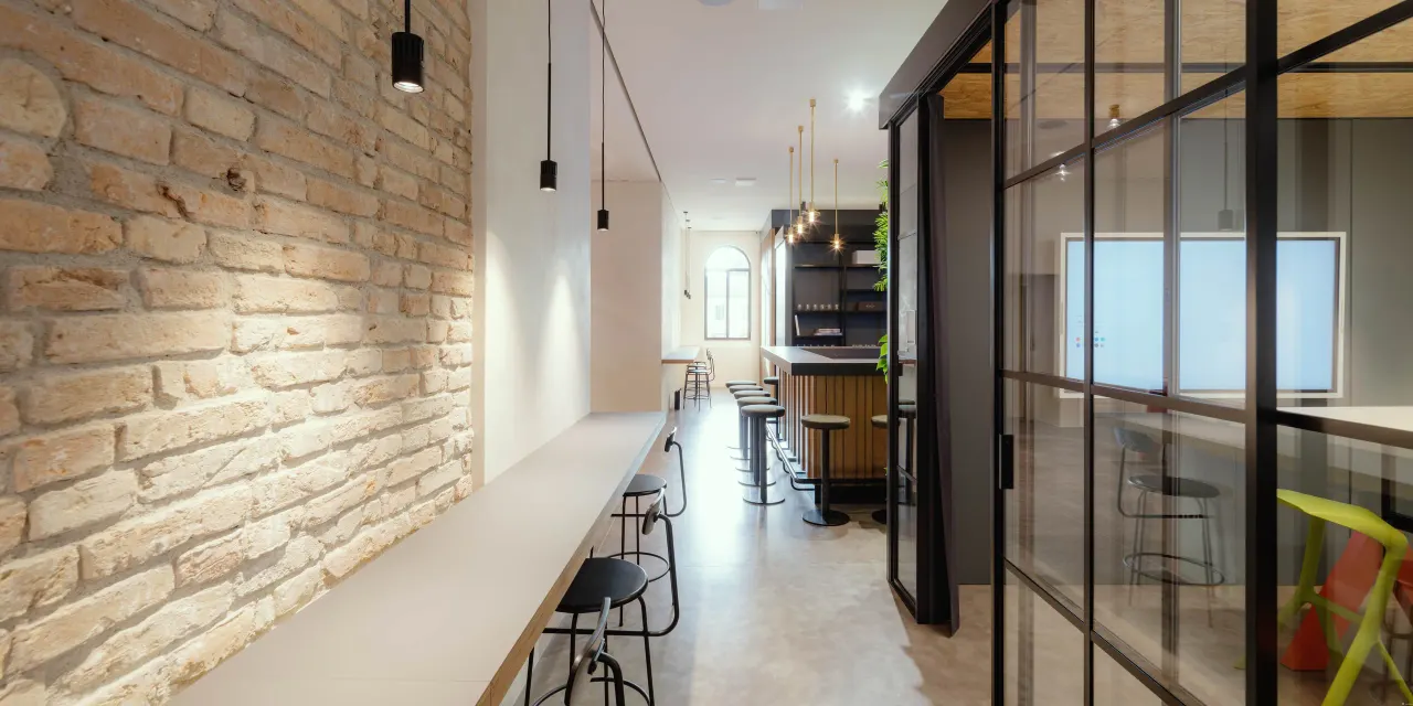 Bar counter along an exposed brick wall beside glazed offices