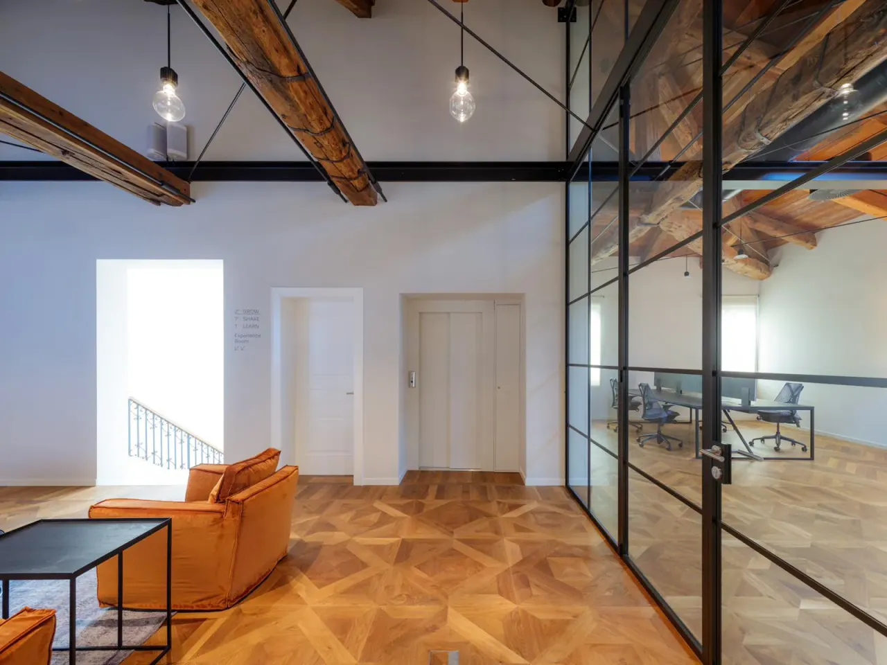 Orange armchairs beside a black-framed glass partition in the attic