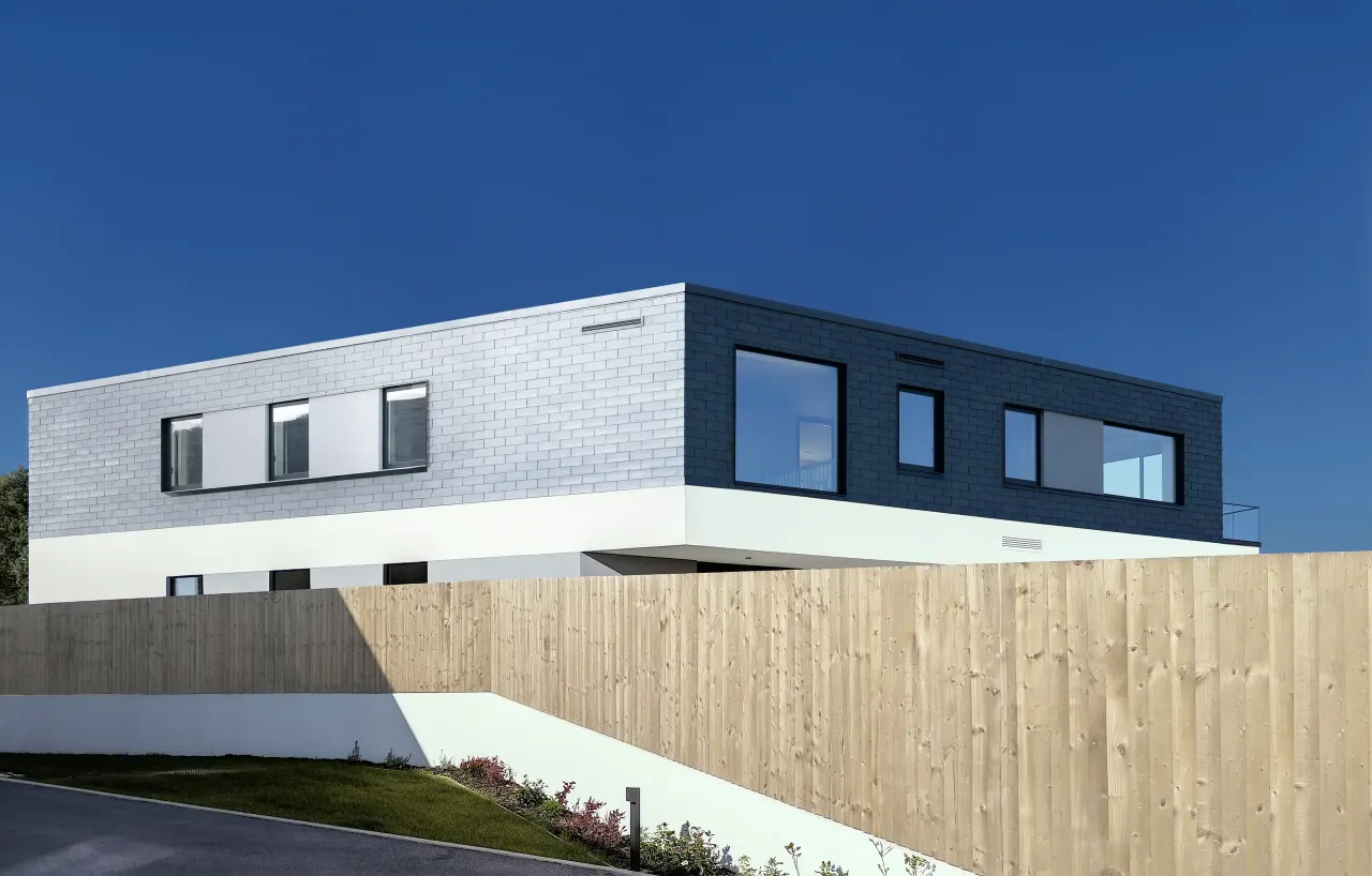 Slate-clad upper floor with long windows above a timber fence